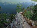 Strmý pohled dolů přes skalní ostroh na hladinu přehrady Vír.